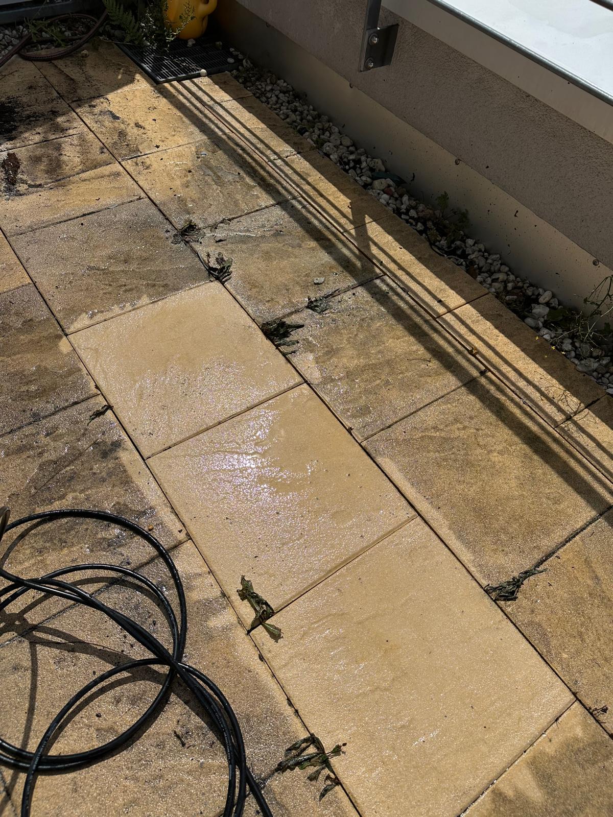 Mehrere gereinigte Terrassenplatten bilden einen hellen Streifen im bestehenden Belag